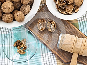 Whole walnuts, shells and kernels in a bowls around a brown wooden board with cracked nuts and wooden meat mallet. Natural