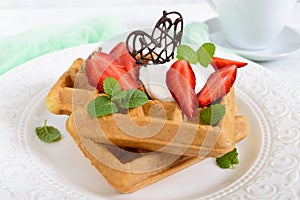 Whole wheat Belgian waffles with whipped cream, freshly chopped strawberries, mint leaves and chocolate and a cup of tea