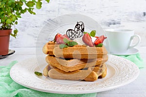 Whole wheat Belgian waffles with whipped cream, freshly chopped strawberries, mint leaves and chocolate and a cup of tea