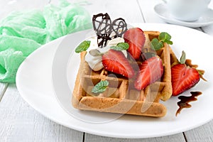 Whole wheat Belgian waffles with whipped cream, freshly chopped strawberries, mint leaves