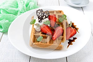 Whole wheat Belgian waffles with whipped cream, freshly chopped strawberries, mint leaves