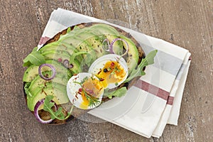 Whole wheat bread Avocado, poached egg sandwich with fresh herbs,red onion on dishcloth wooden board background. Healthy photo