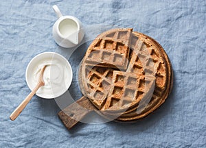 Whole wheat breakfast viennese waffles, cream and milk on blue background