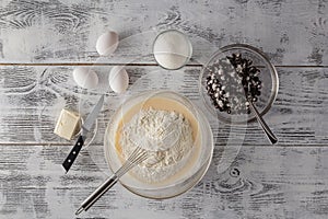 Whole-wheat flour in white bowl, milk, eggs on a light wooden ba