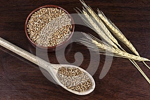 Whole wheat grains in a wooden spoon and a ceramic bowl on a wooden table