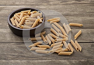 Whole wheat penne pasta on a bowl over wooden table