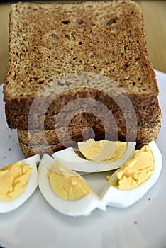 Whole wheat slice toasted bread with sliced boiled egg on the white plate for breakfast