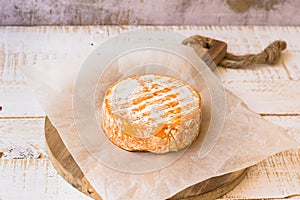 Whole wheel of soft French, German cheese with orange rind with mold on parchment paper, wood cutting board, concrete wall