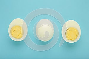 Whole white egg and halved boiled egg with yolk on blue background