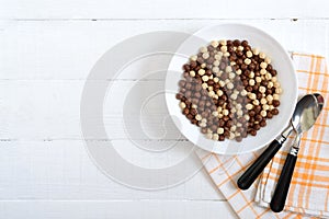 Wholegrain chocolate and milk balls in bowl on white wooden background. Healthy cereal breakfast. Baby breakfast. Baby eating. photo