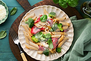 Wholegrain pasta penne with broccoli and red grilled bell pepper and on light wooden rustic background table. Vegan pasta. Italian