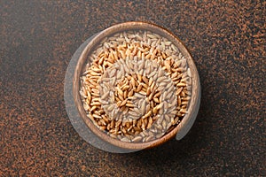 Wholegrain spelt farro in wooden bowl on brown background. Top view