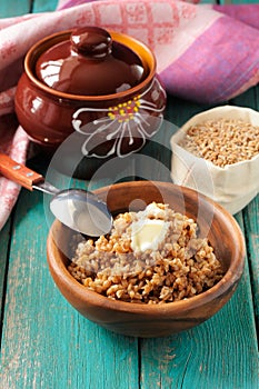 Wholegrain spelt porridge with butter in wooden bowl and raw spelt in linen bag on wooden table