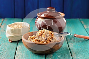 Wholegrain spelt porridge with butter in wooden bowl and raw spelt in linen bag on wooden table