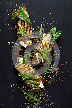 Wholemeal bread sandwiches with feta cheese, grilled zucchini, green asparagus, sugar peas, olive oil on a black background