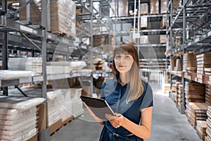 Wholesale warehouse. Beautiful young woman worker of store in shopping center. Girl looking for goods with a tablet is