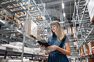 Wholesale warehouse. Beautiful young woman worker of store in shopping center. Girl looking for goods with a tablet is