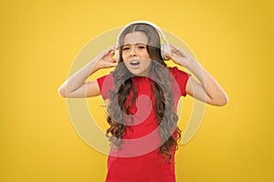 Why do my headphones sound low. Little girl wearing headphones on yellow background. Cute child listening to music in