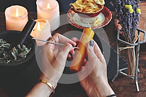 Wiccan witch carving symbols and sigils onto yellow gold color candlestick at her altar