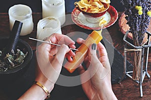 Wiccan witch carving symbols and sigils onto yellow gold color candlestick at her altar