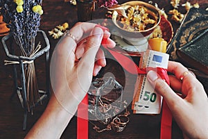 Wiccan witch casting money spell at her altar - tying red ribbon around yellow candle with money banknotes using her hands