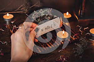 Wiccan witch holding a piece of paper with words So mote it be written on it, and burning it at her altar. Witch casting a spell