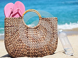 Wicker bag with flip flops on the beach next to a plastic water bottle. background sand