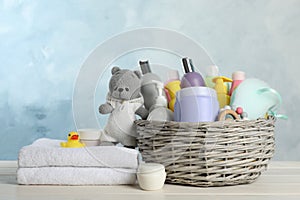 Wicker basket with baby cosmetic products, towel and toys on white wooden table
