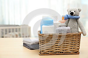 Wicker basket with baby cosmetic products, toy and towels on table indoors.