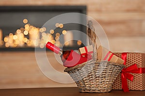 Wicker basket with bottle of wine and gift boxes on table in room