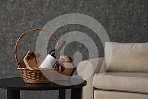 Wicker basket with bottle of wine and gift boxes on table in room