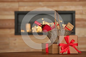 Wicker basket with bottle of wine and gift boxes on table in room