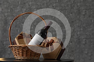 Wicker basket with bottle of wine and gift boxes on table