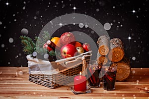 Wicker basket with bottles of wine, bottle of champagne,  christmas decorations and fruits. Mulled wine, candle and firewood