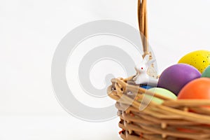 Wicker basket with bright colorful eggs and with text Happy Easter and flower