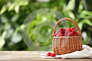 Wicker basket with delicious ripe raspberries on table against blurred background, space for text