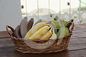 Wicker basket with different sorts of bananas on wooden table