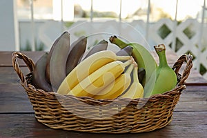 Wicker basket with different sorts of bananas on wooden table