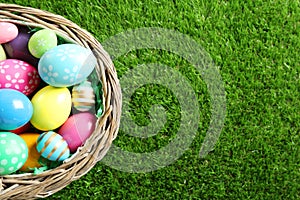 Wicker basket with Easter eggs on green grass, top view. Space for text