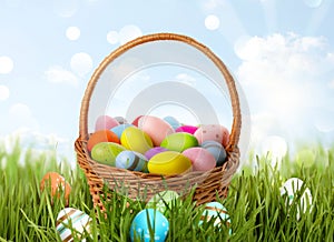 Wicker basket with festively decorated Easter eggs in green grass on sunny day