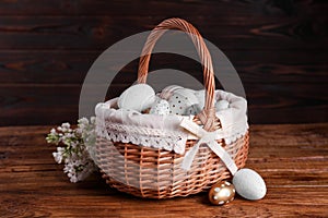 Wicker basket with festively decorated Easter eggs and white lilac flowers on wooden table