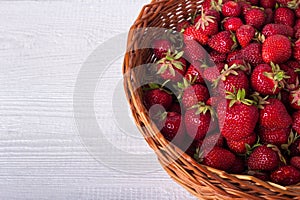 Wicker basket filled with ripe strawberries. On a white wooden background. Copy-space.