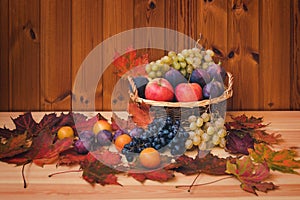 Wicker basket with fresh fruits and autumn maple leaves on wooden background.