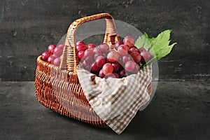Wicker basket with fresh red grapes on grey background