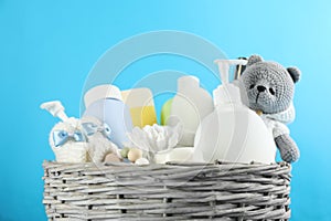 Wicker basket full of baby cosmetic products, bathing accessories and toy on light blue background, closeup