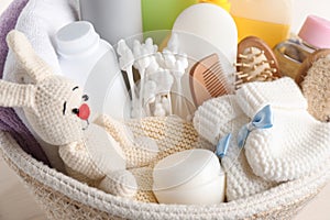 Wicker basket full of different baby cosmetic products, bathing accessories and toy on table, closeup