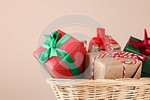 Wicker basket full of gift boxes on beige background, closeup