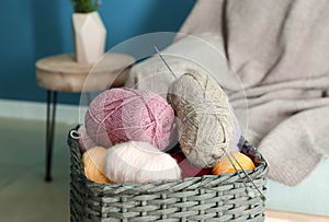 Wicker basket with knitting yarn and needles in room
