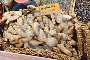 Wicker basket with lots of bresco ginger and a sign with the price in euros per hundred grams surrounded by other spices