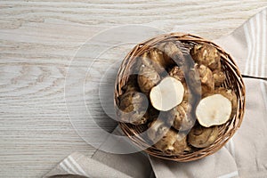 Wicker basket with many Jerusalem artichokes on white wooden table, top view. Space for text